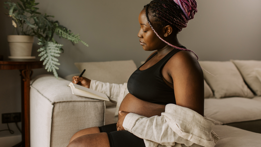 Woman with pink-accented braids journaling on a sofa in a quiet moment of reflection and everyday self-care